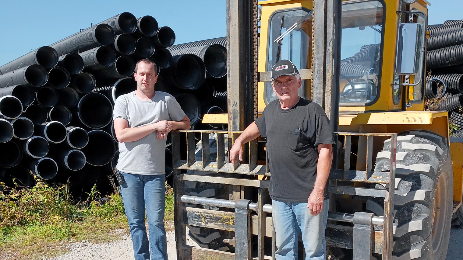 2 men standing next to pipe and construction vehicle